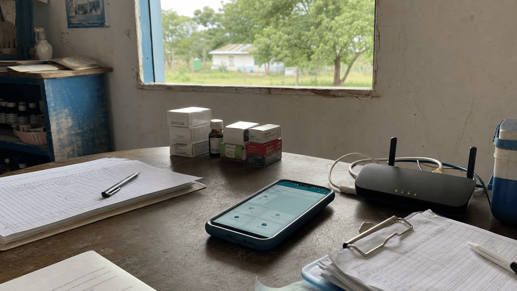 Mesa de clínica rural con formularios, medicamentos, teléfono y router local para trabajo sin conexión